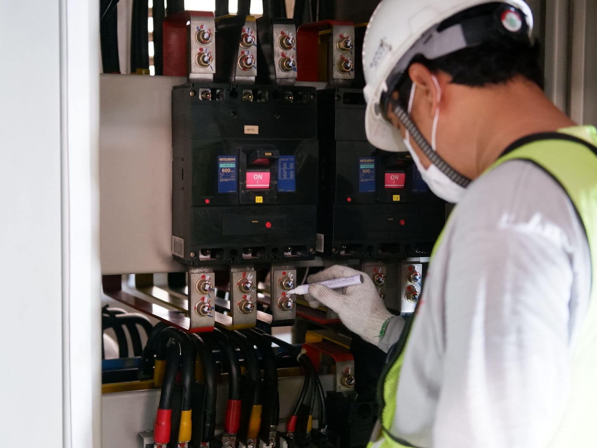 Technician in a hard hat checking circuit breakers in an electrical switchgear cabinet