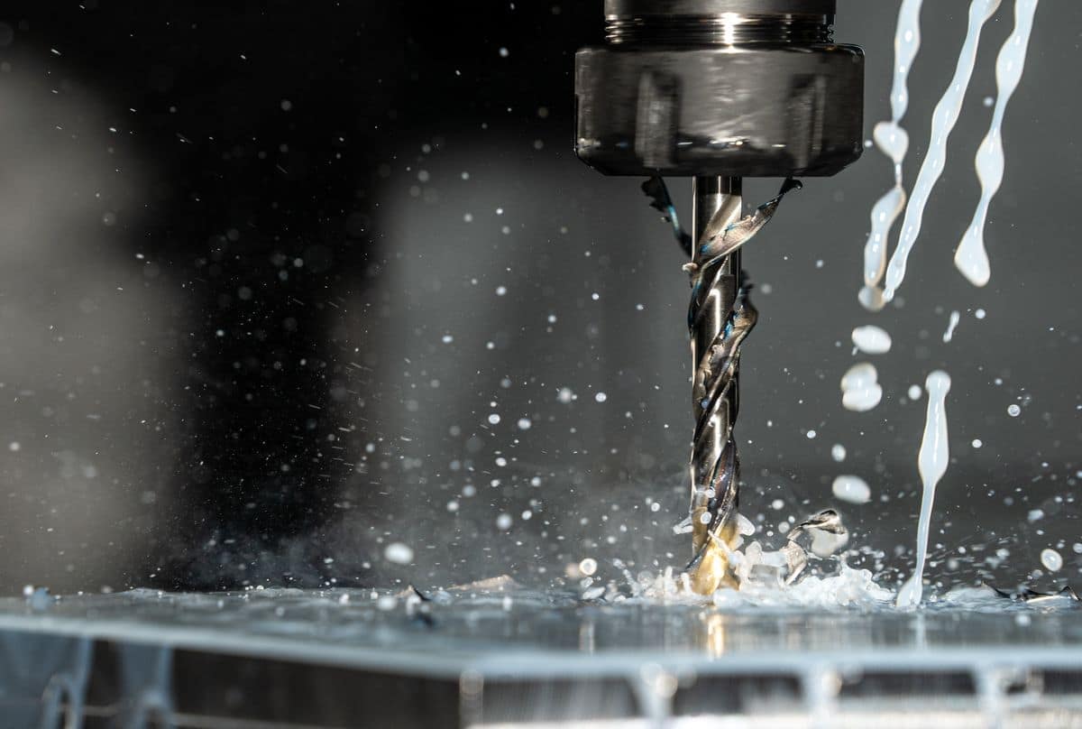 Broca CNC mecanizando una pieza metálica con refrigerante salpicando