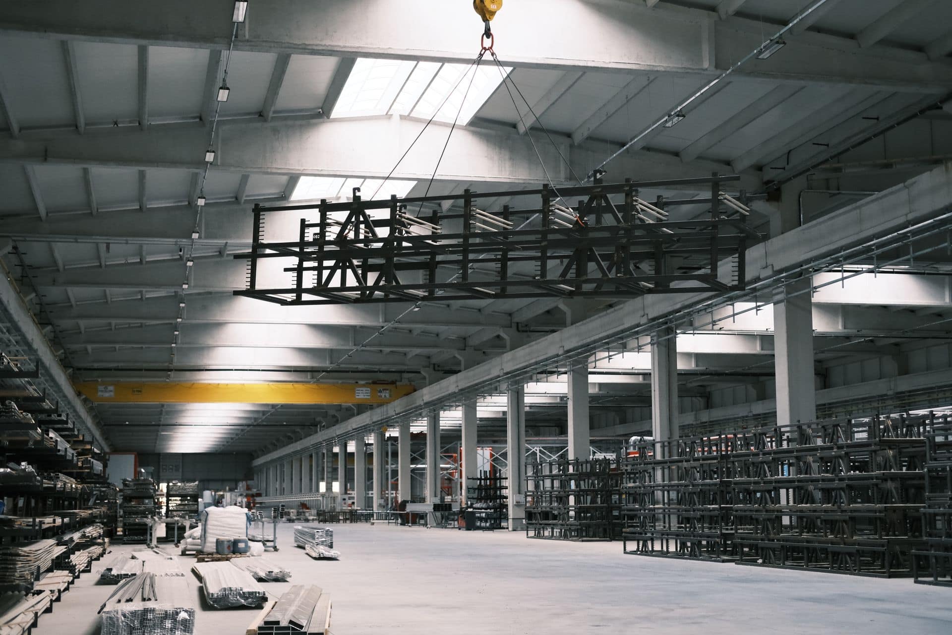 Overhead crane lifting a steel rack through a large industrial hall