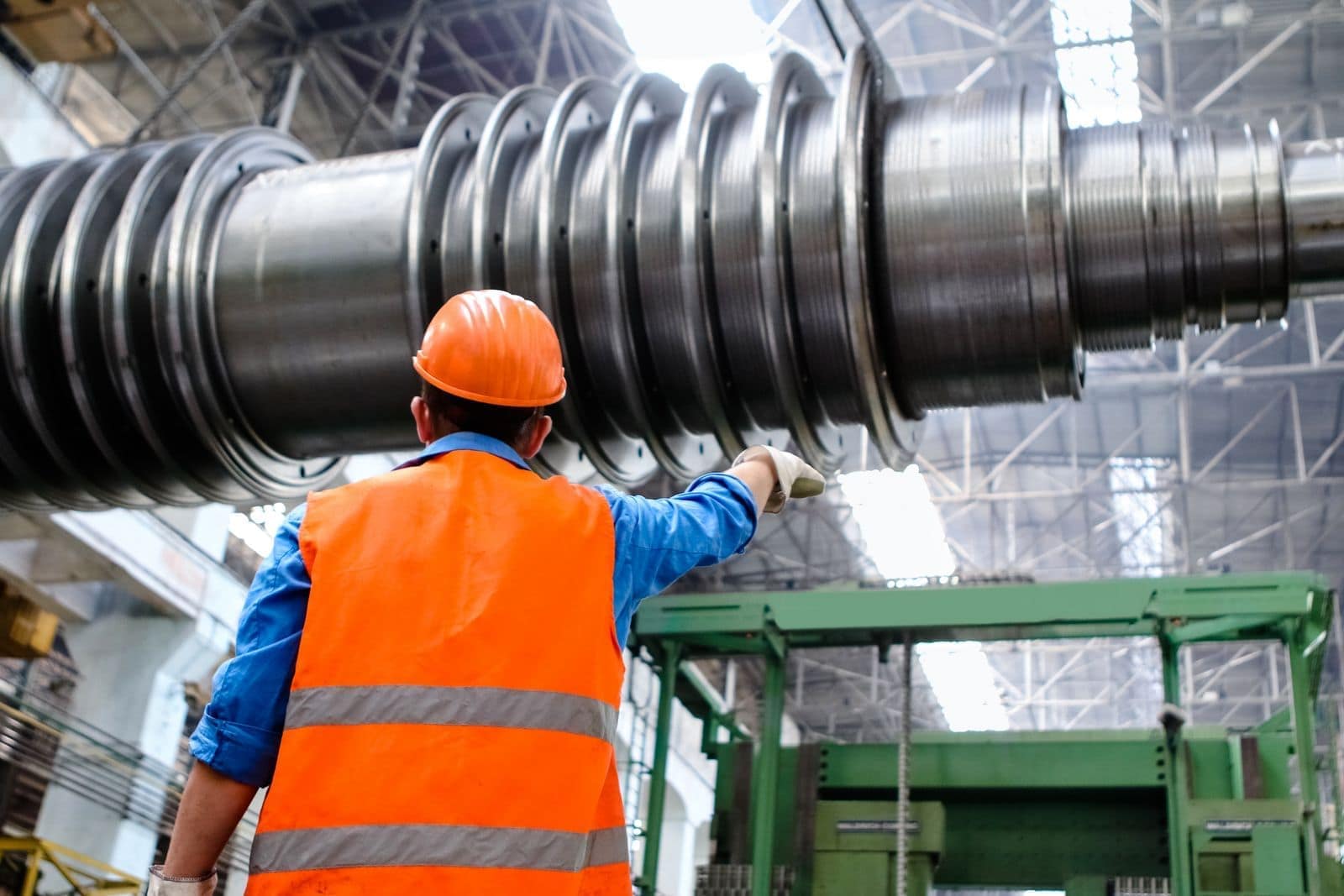 Ingegnere in un capannone di costruzione macchine indica un grande albero di turbina