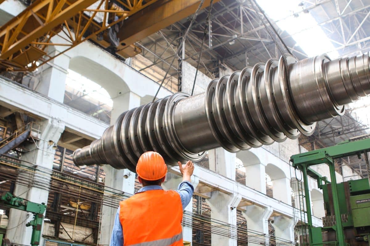 Ingegnere con gilet ad alta visibilità sotto un grande albero di turbina in un capannone di produzione