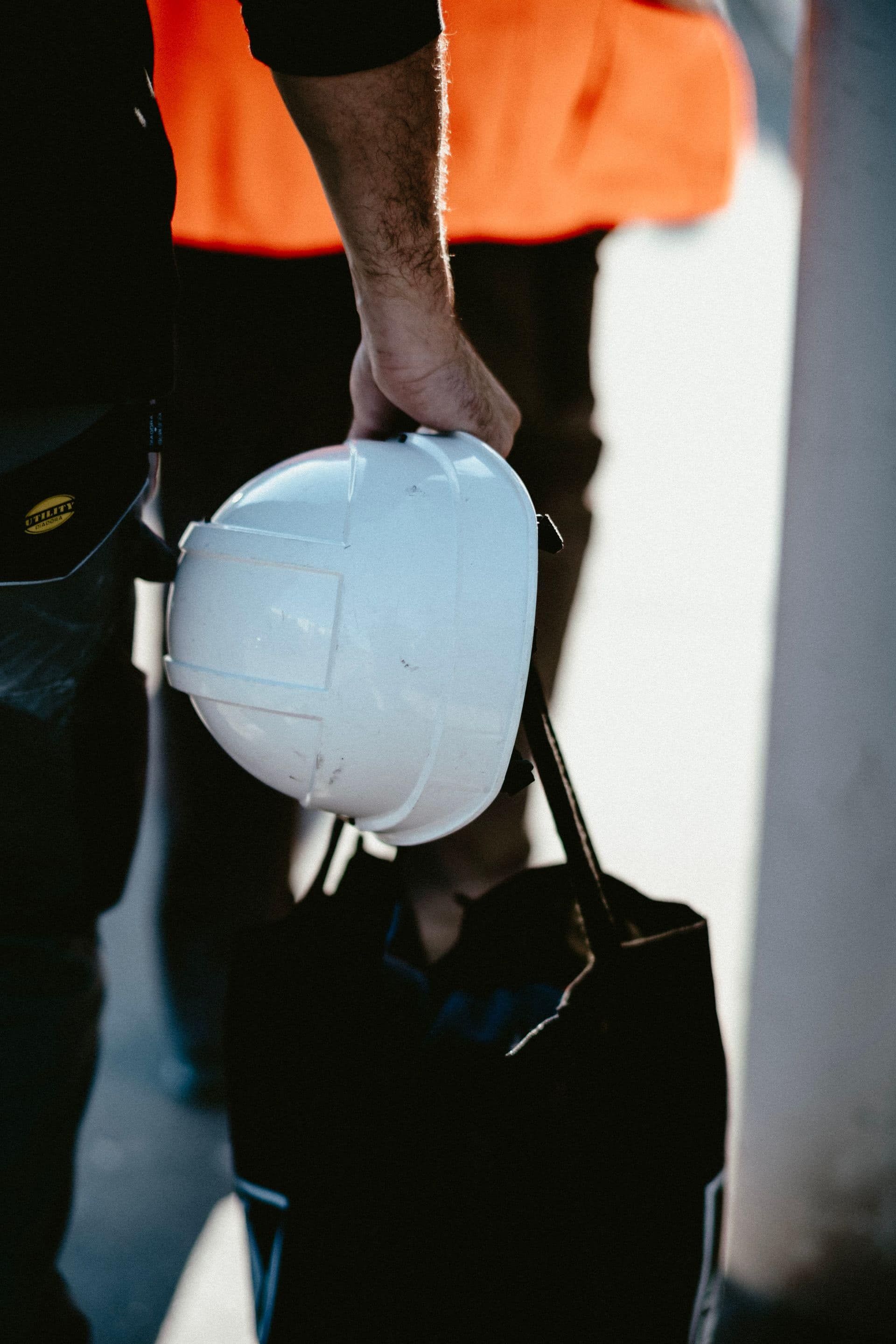 Worker in a high-visibility vest carrying a hard hat and a tool bag