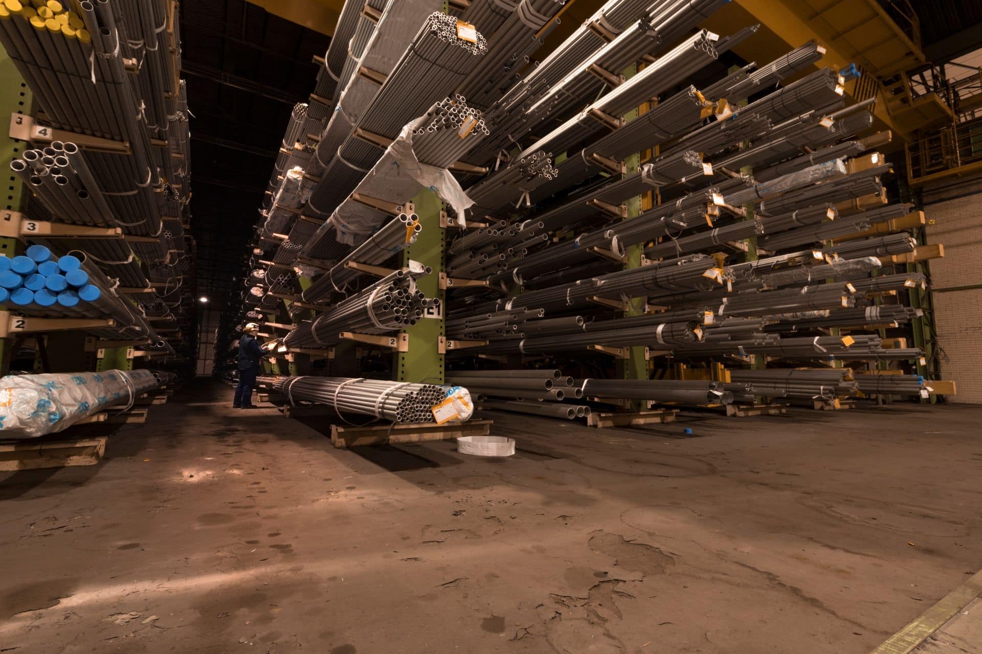 Worker between cantilever racks stacked with steel tubes in a distribution warehouse